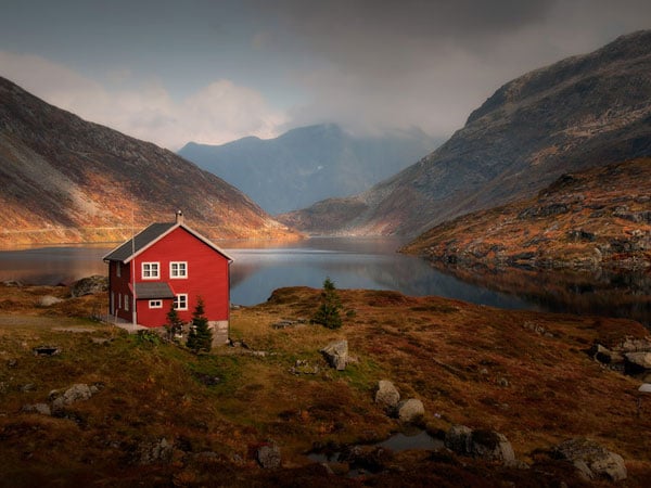 This house with red exterior may have a unique purpose. It can be easily identified in this wilderness. It sticks out and helps the owner to get home easily or stranded hikers to easily ask for help if needed. red house by lake and mountain - Feng Shui Colors: The Science and Psychology Behind It